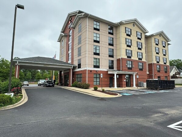 A multi-story hotel with a covered entrance, parking area, and a flag.