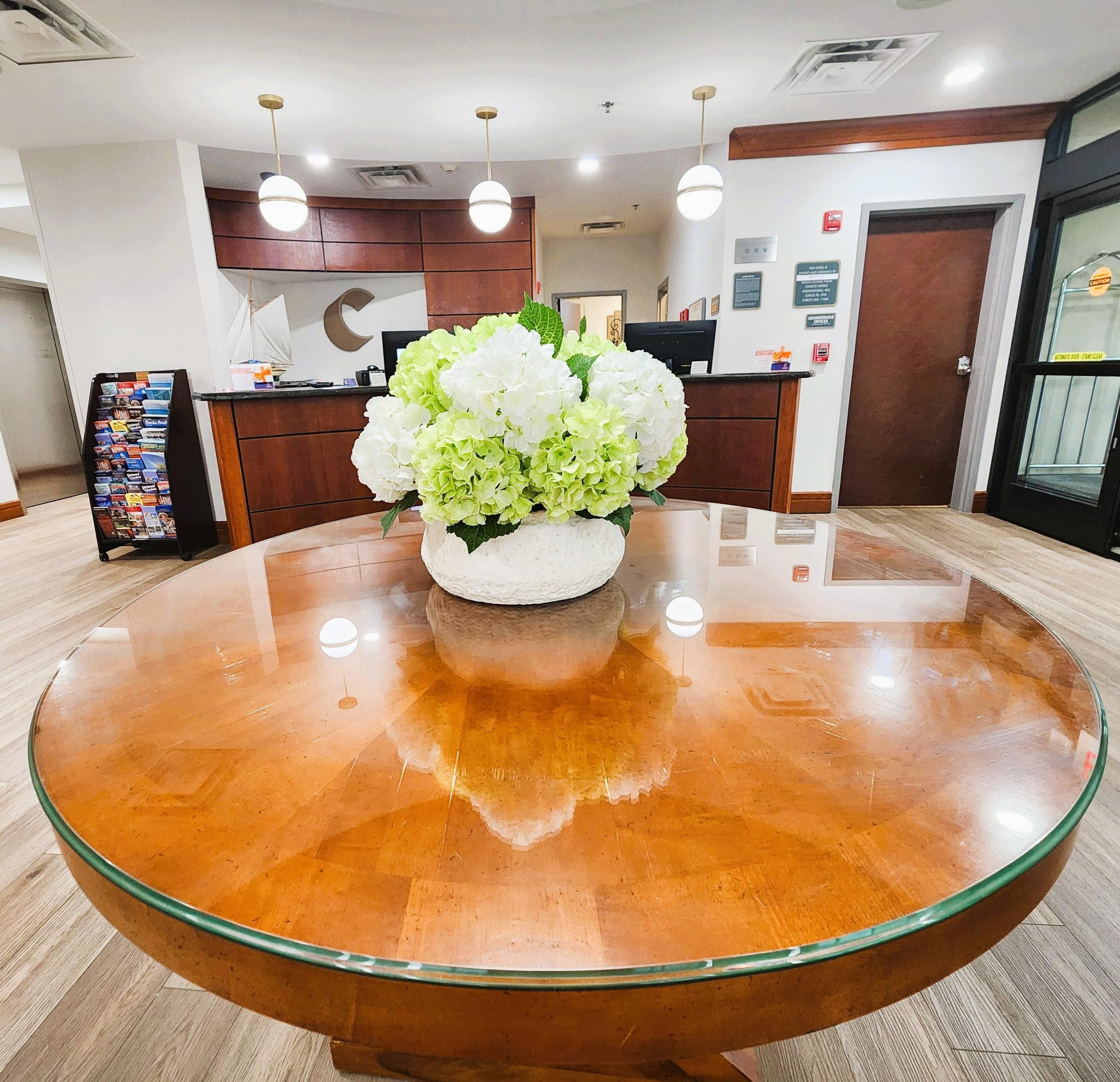 Un área de recepción con una mesa redonda de cristal, un arreglo floral, una recepción y un detector de incendios en la pared.