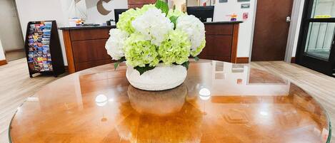 Un área de recepción con una mesa redonda de cristal, un arreglo floral, una recepción y un detector de incendios en la pared.