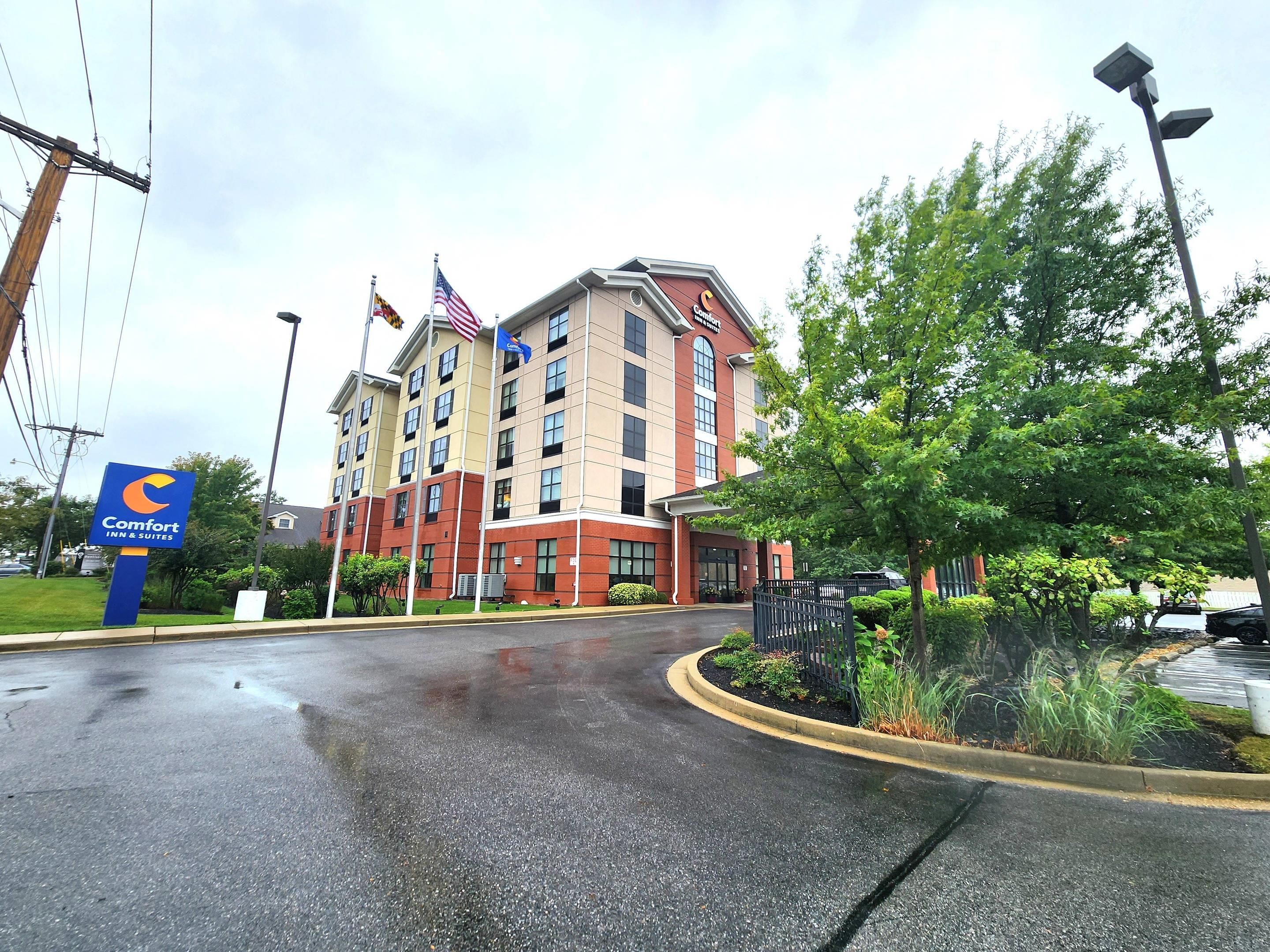Un hôtel Comfort Inn & Suites avec une façade rouge et beige, plusieurs drapeaux et un parking mouillé.