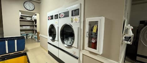 A laundry room with two front-loading washers, a clock, and a fire extinguisher.