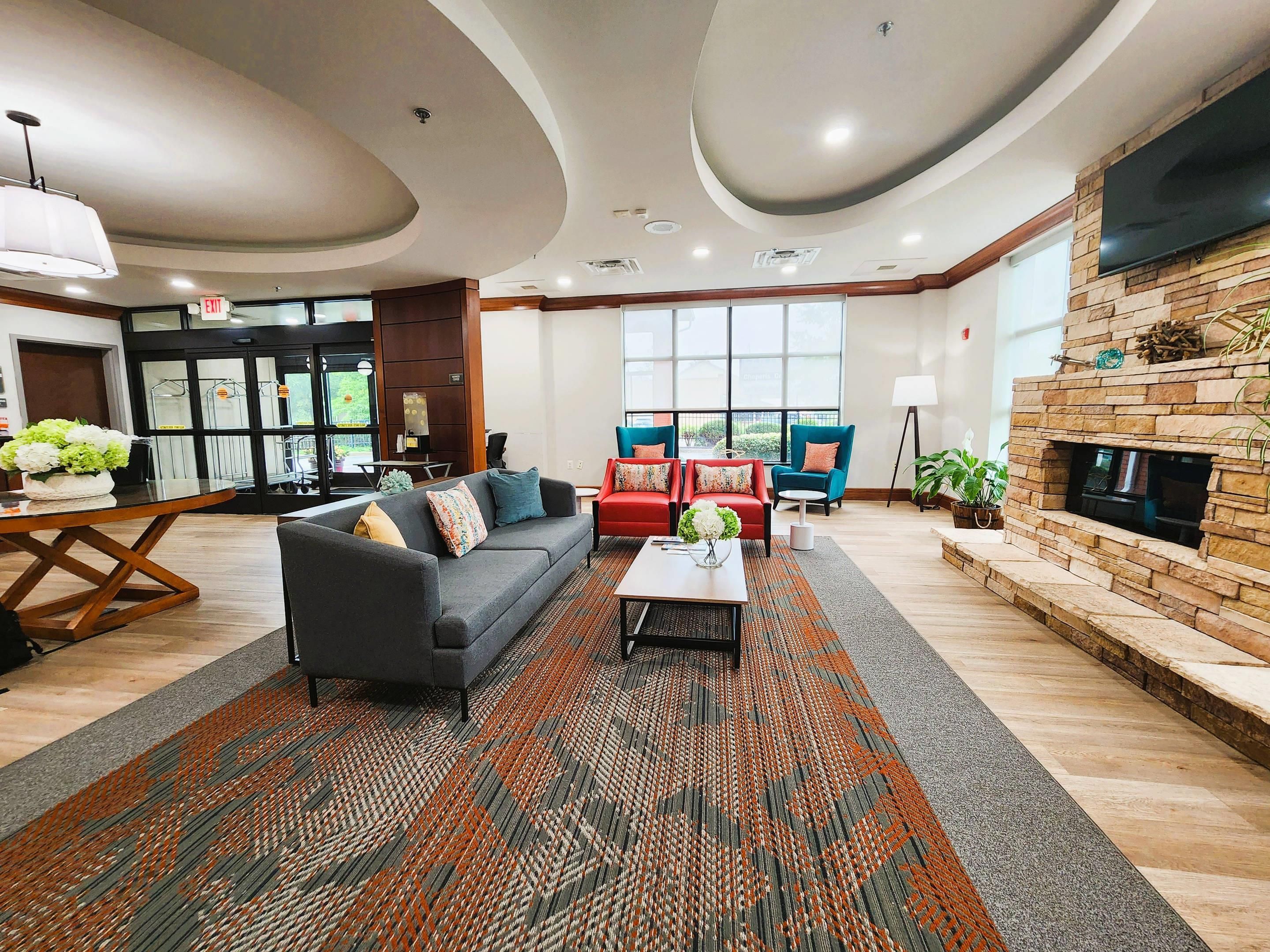 A modern hotel lobby with a sofa, chairs, a fireplace, and a large window.