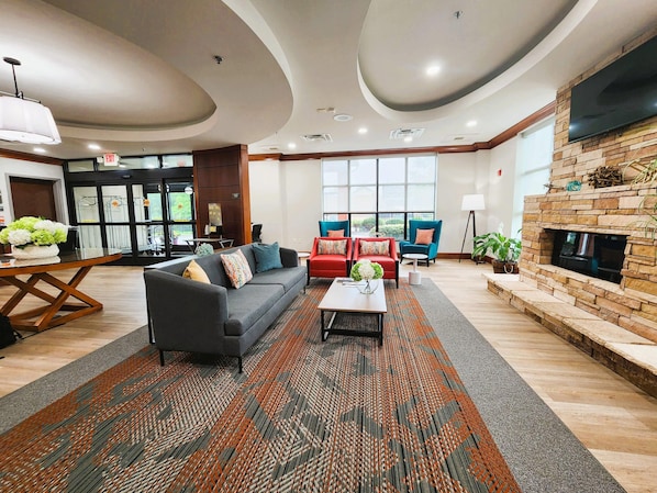 A modern hotel lobby with a sofa, chairs, a fireplace, and a large window.