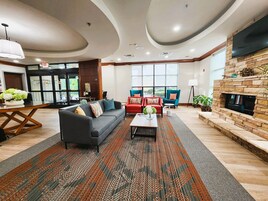 A modern hotel lobby with a sofa, chairs, a fireplace, and a large window.