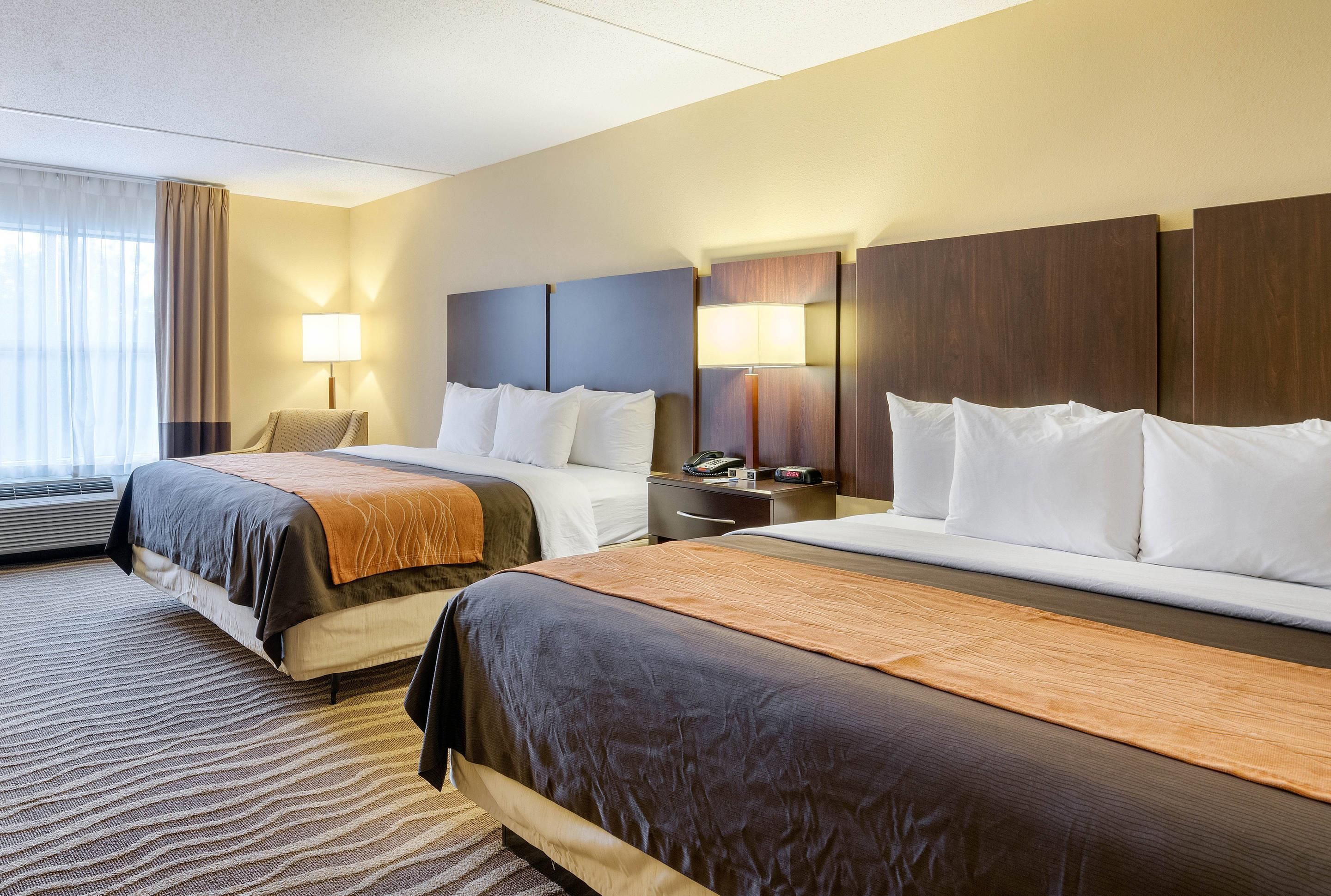 A hotel room with two beds, a desk, a chair, and a window with curtains.