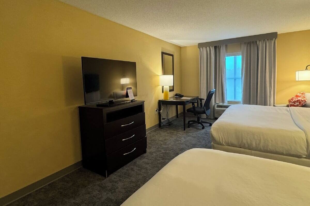 A hotel room with two beds, a desk with a chair, a television, and a dresser.