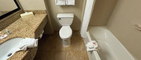 A bathroom with a granite countertop sink, a toilet, and a bathtub.
