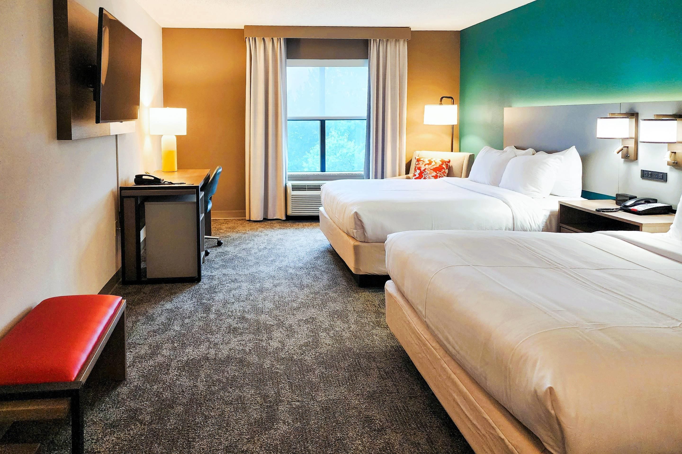 Une chambre d’hôtel avec deux lits, un bureau, une chaise, une télévision et une fenêtre avec des rideaux.