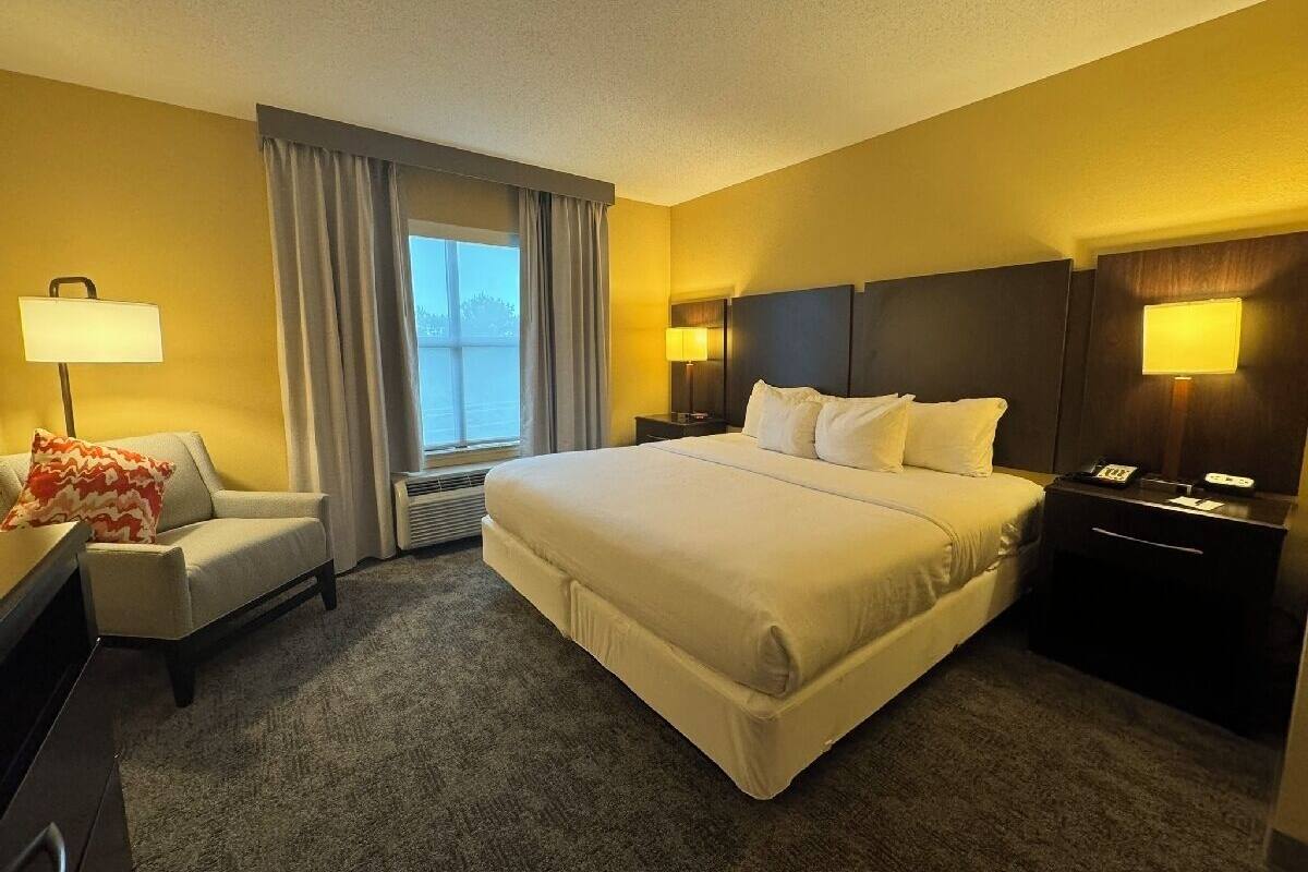 A hotel room with a large bed, a desk, a chair, and a nightstand with a lamp.