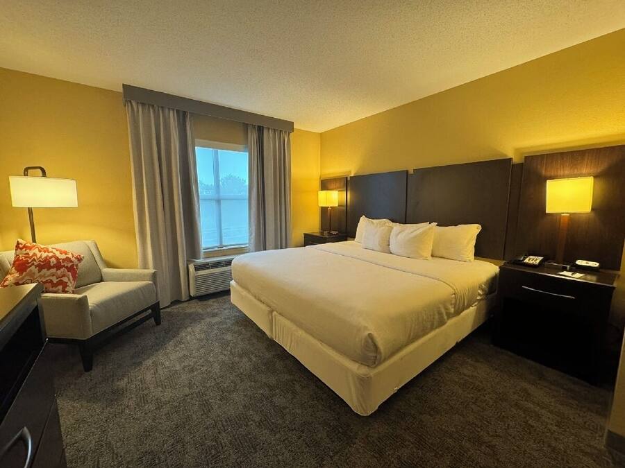 A hotel room with a large bed, a desk, a chair, and a nightstand with a lamp.