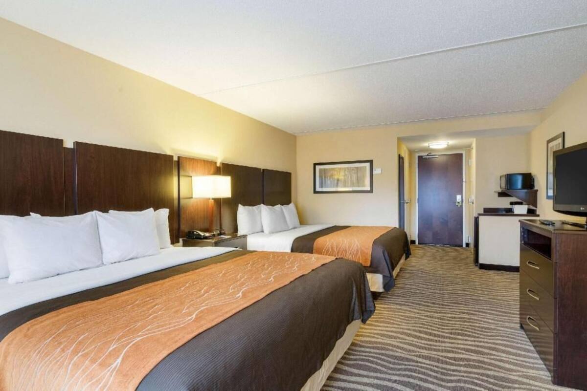 A hotel room with two beds, a desk, a television, and a door leading to another room.