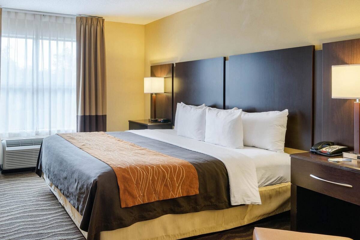 A hotel room with a bed, bedside lamps, a desk with a phone, and a window with curtains.