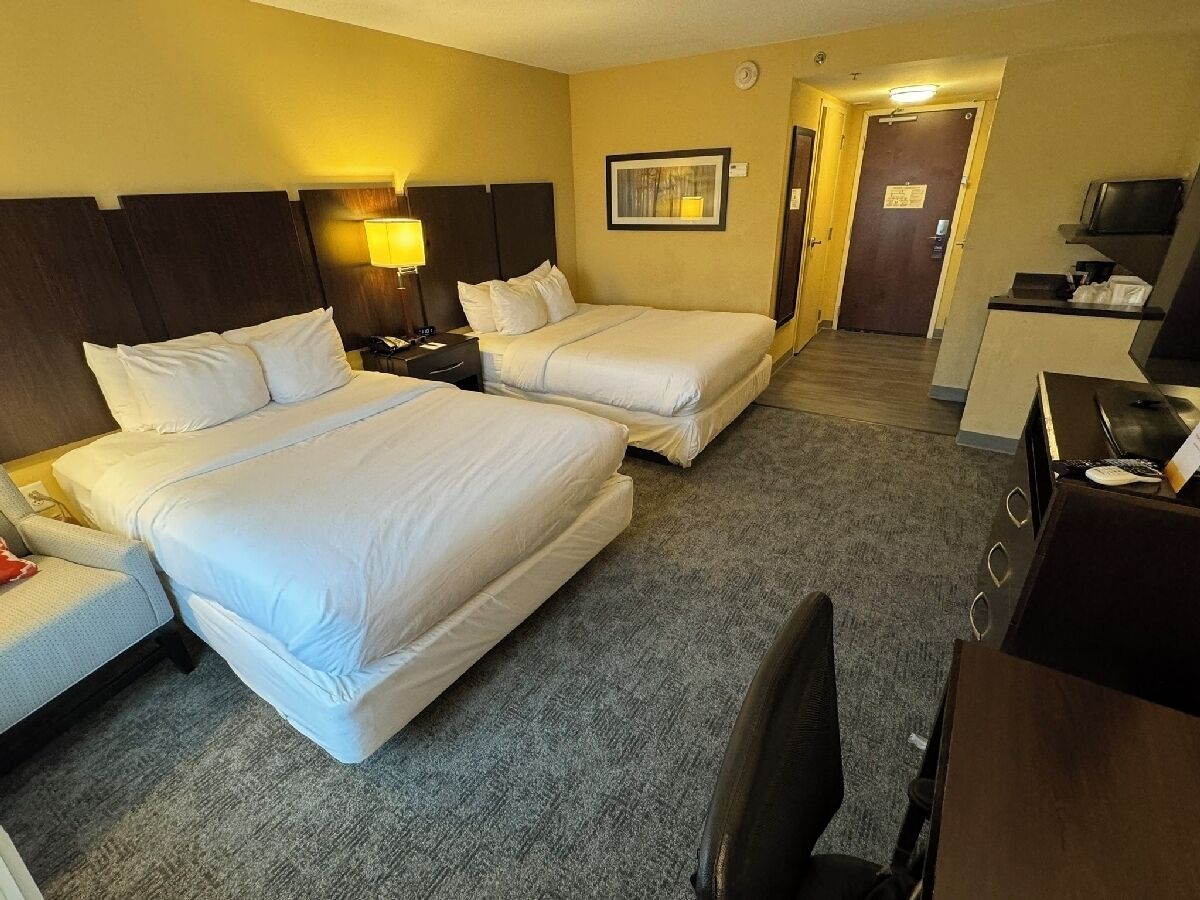 A hotel room with two beds, a desk, a chair, a lamp, and a television.