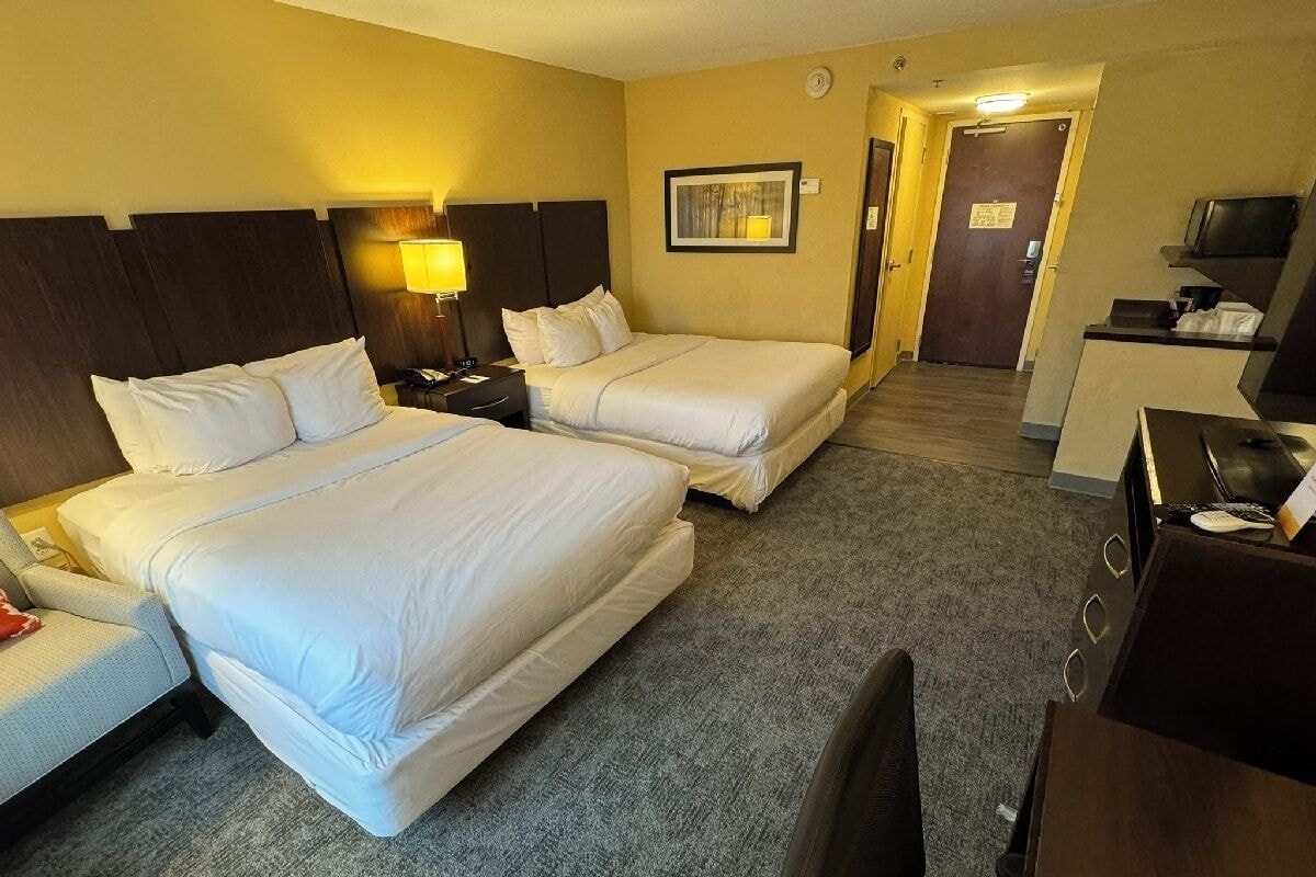 A hotel room with two beds, a desk, a chair, a lamp, and a television.