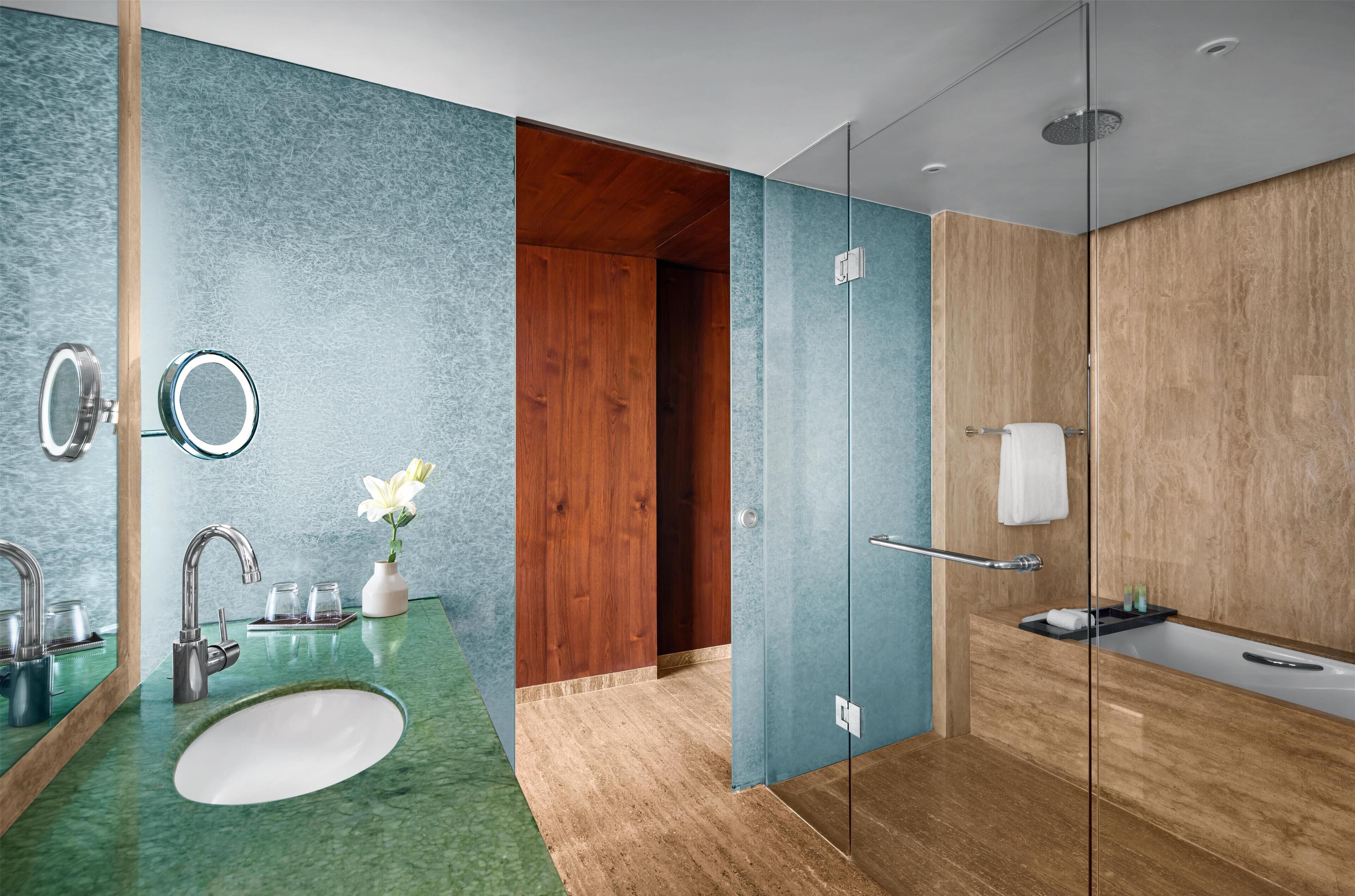Un baño moderno con lavamanos de mármol verde, puerta de madera y cabina de ducha de vidrio.