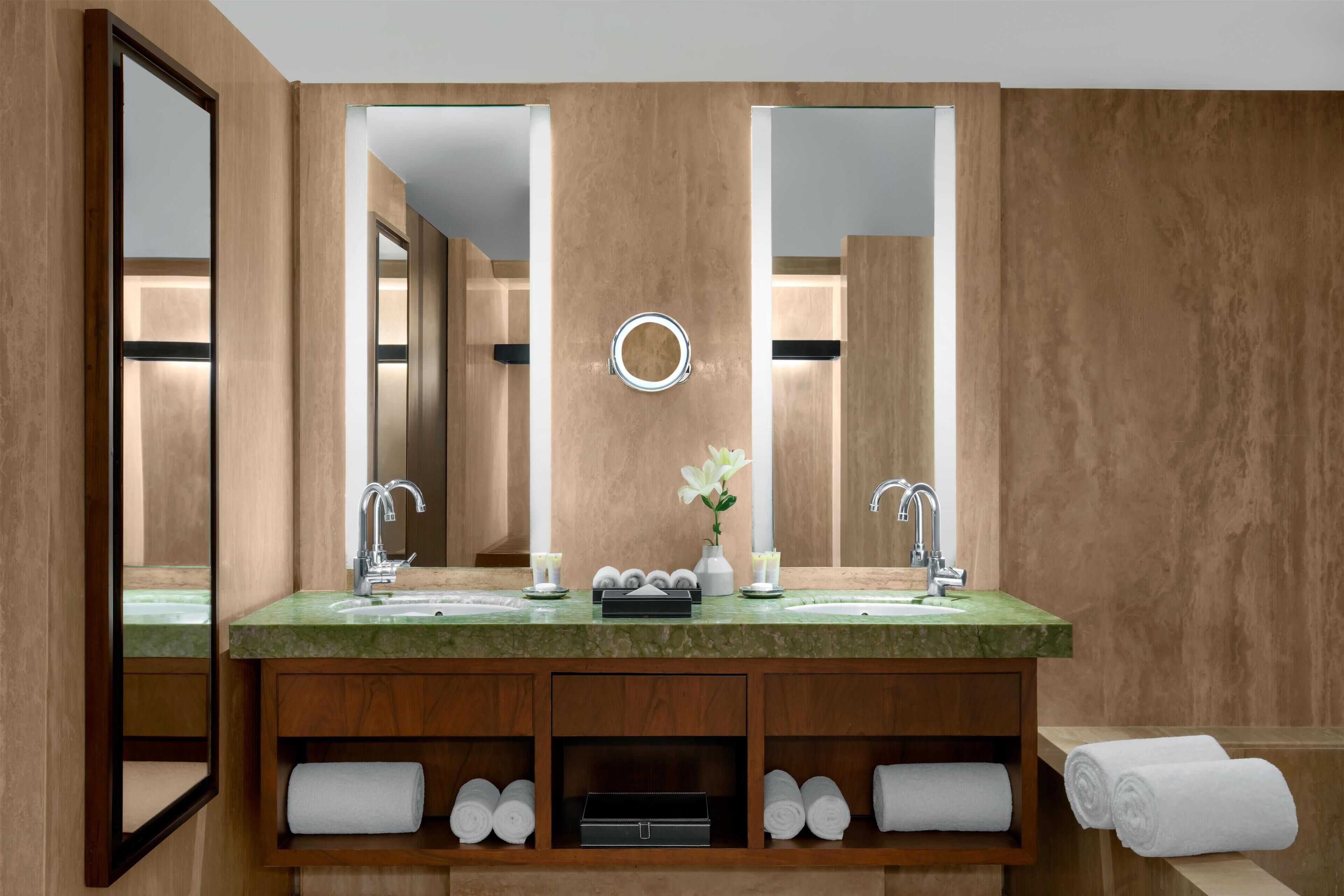 A modern bathroom with a large mirror, two sinks, and a vanity with shelves for towels.