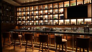 A bar area with multiple shelves of bottles, a counter, and bar stools.
