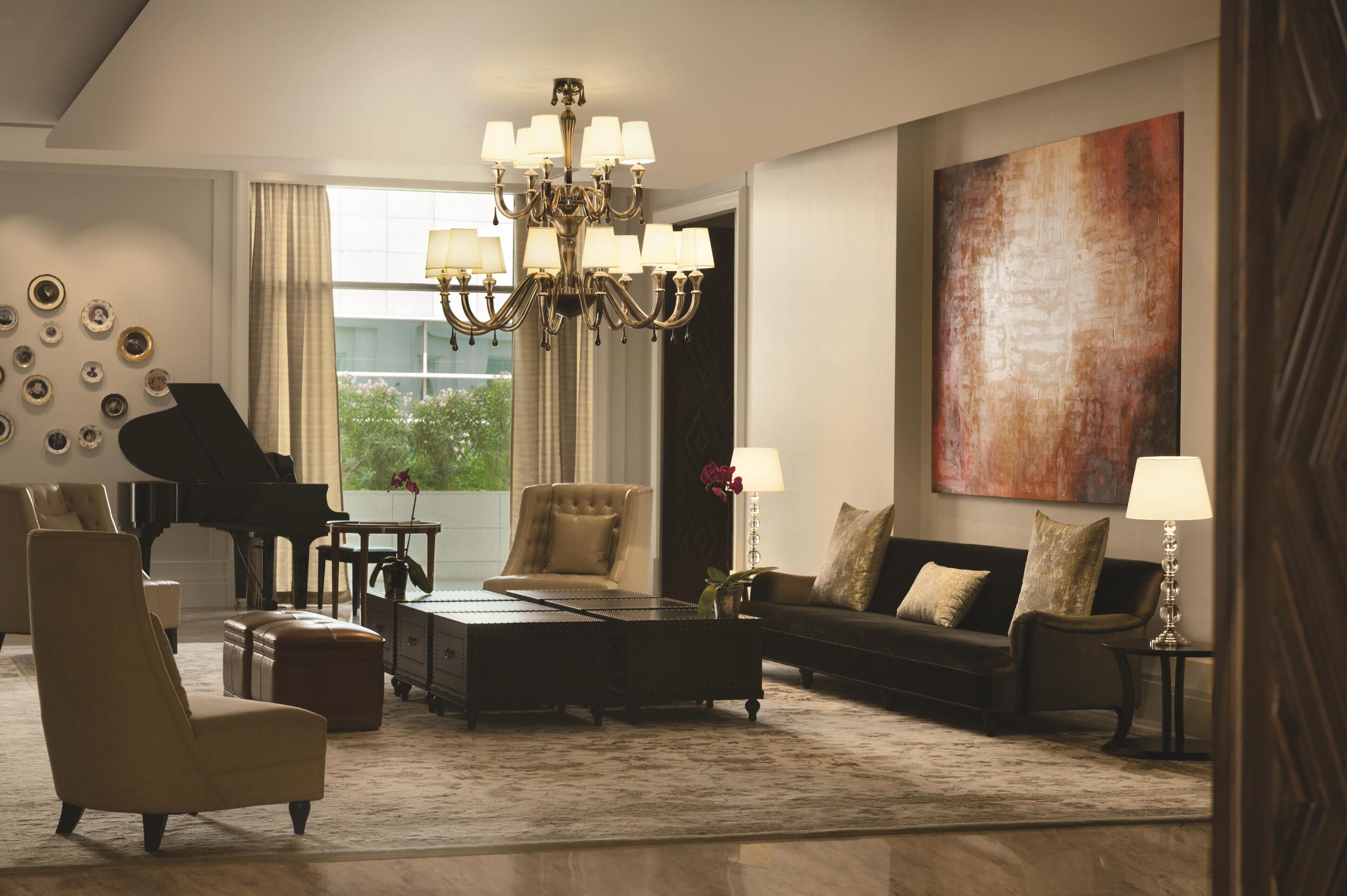 A spacious living room with a grand piano, a chandelier, a sofa set, and a large abstract painting.