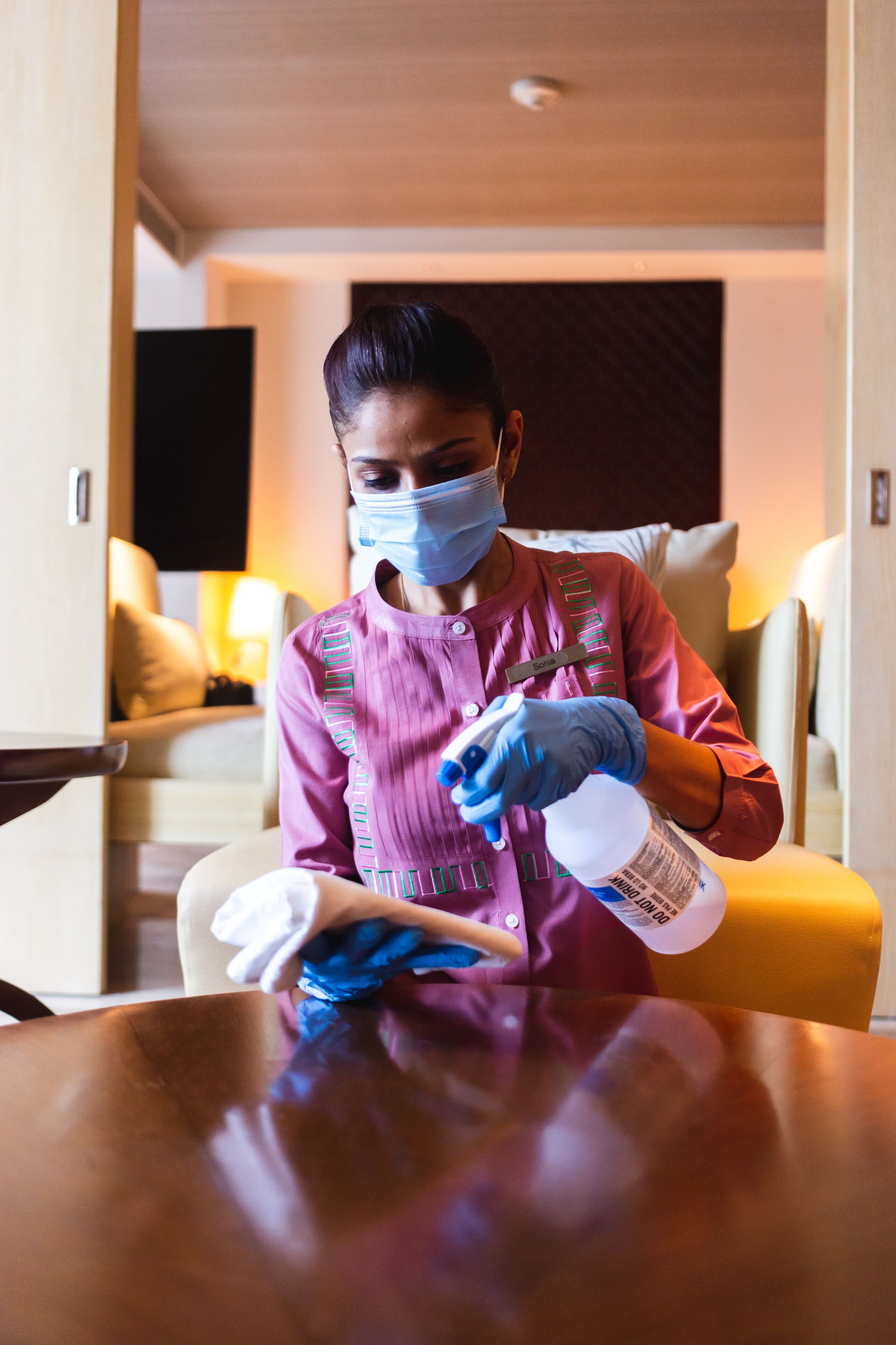 A person cleaning a table with a spray bottle and cloth in a hotel room.