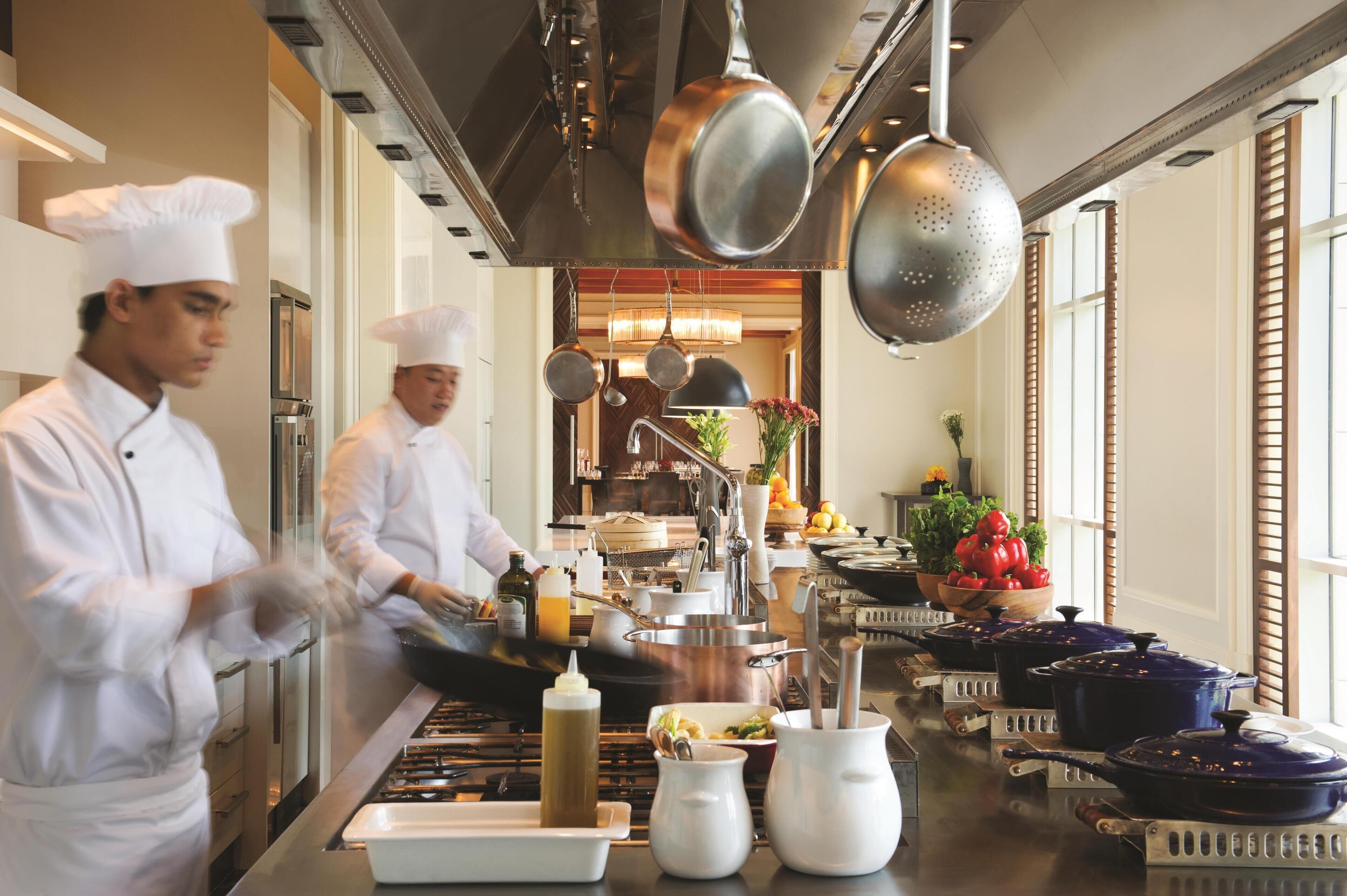 A professional kitchen with chefs preparing food, stainless steel appliances, and various cooking utensils.