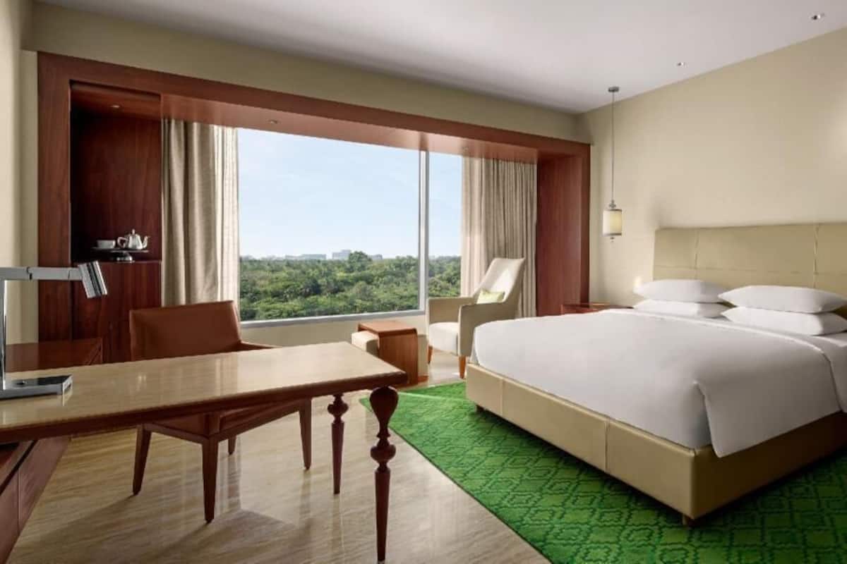 A hotel room with a large bed, a desk, a chair, a nightstand, and a view of the outdoors.
