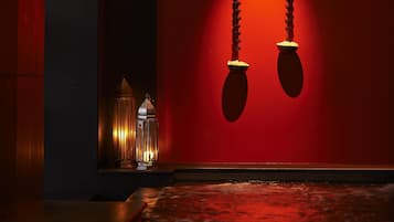 A dimly lit room with a red wall, a hanging light fixture, and a small table with a lamp.