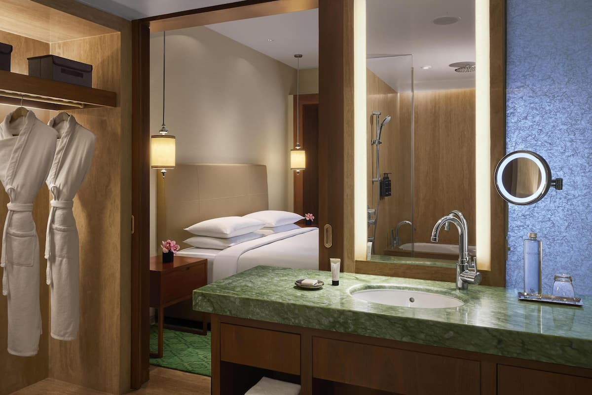 A hotel bathroom with a large mirror, a sink with a green marble countertop, and a shower area.
