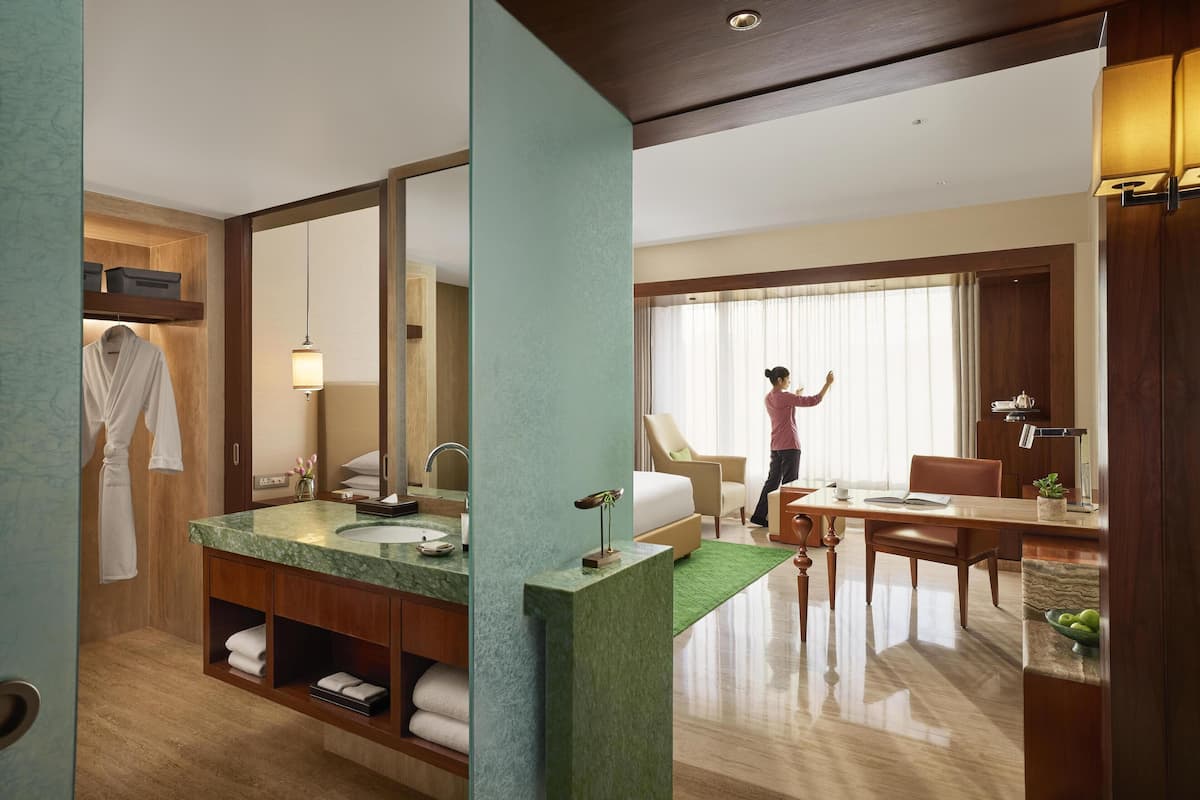 A hotel room with a marble bathroom, a dining area with a table and chairs, and a large window with curtains.