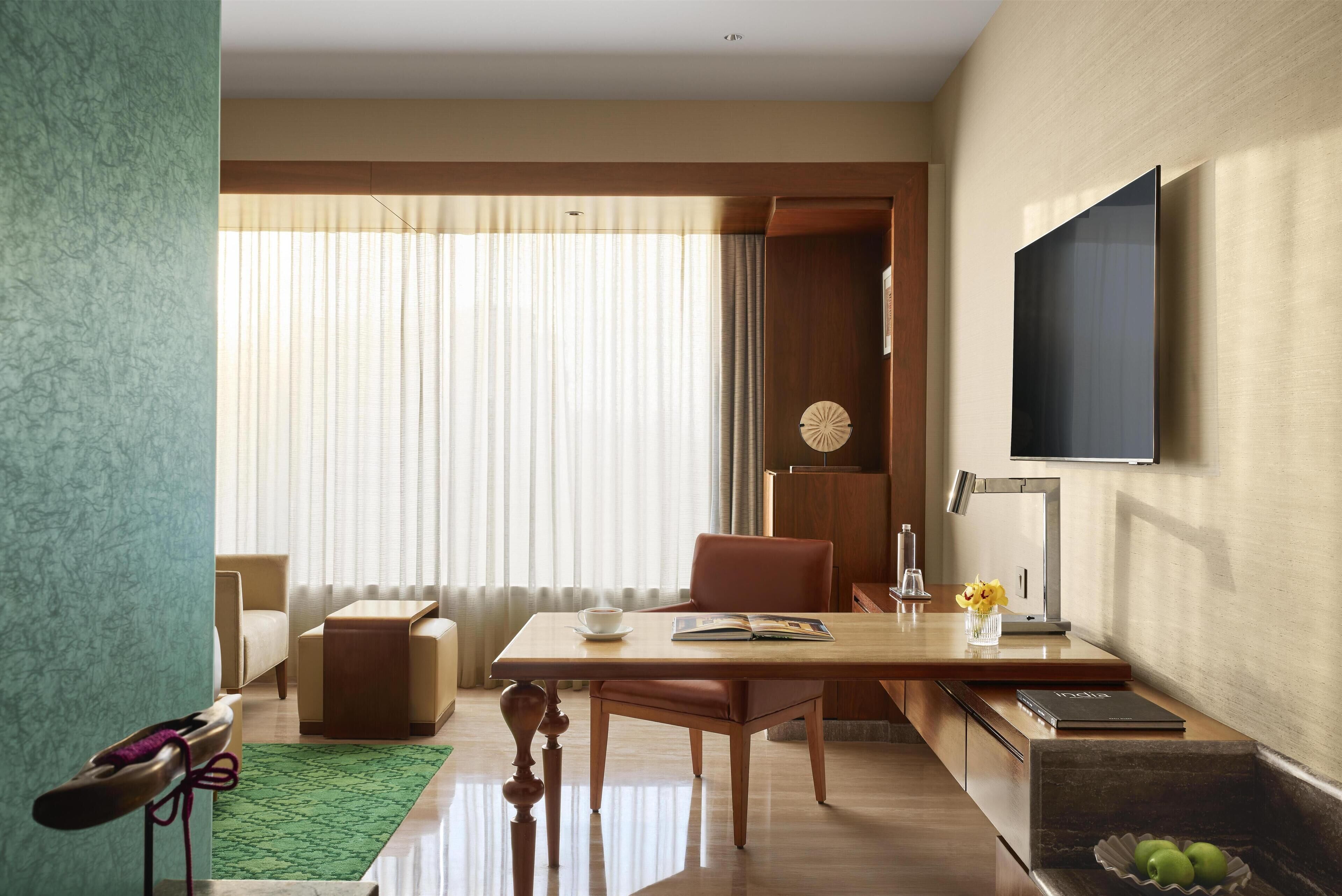 A modern living room with a wooden table, a sofa, a TV mounted on the wall, and a large window with curtains.