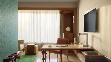 A modern living room with a wooden table, a sofa, a TV mounted on the wall, and a large window with curtains.
