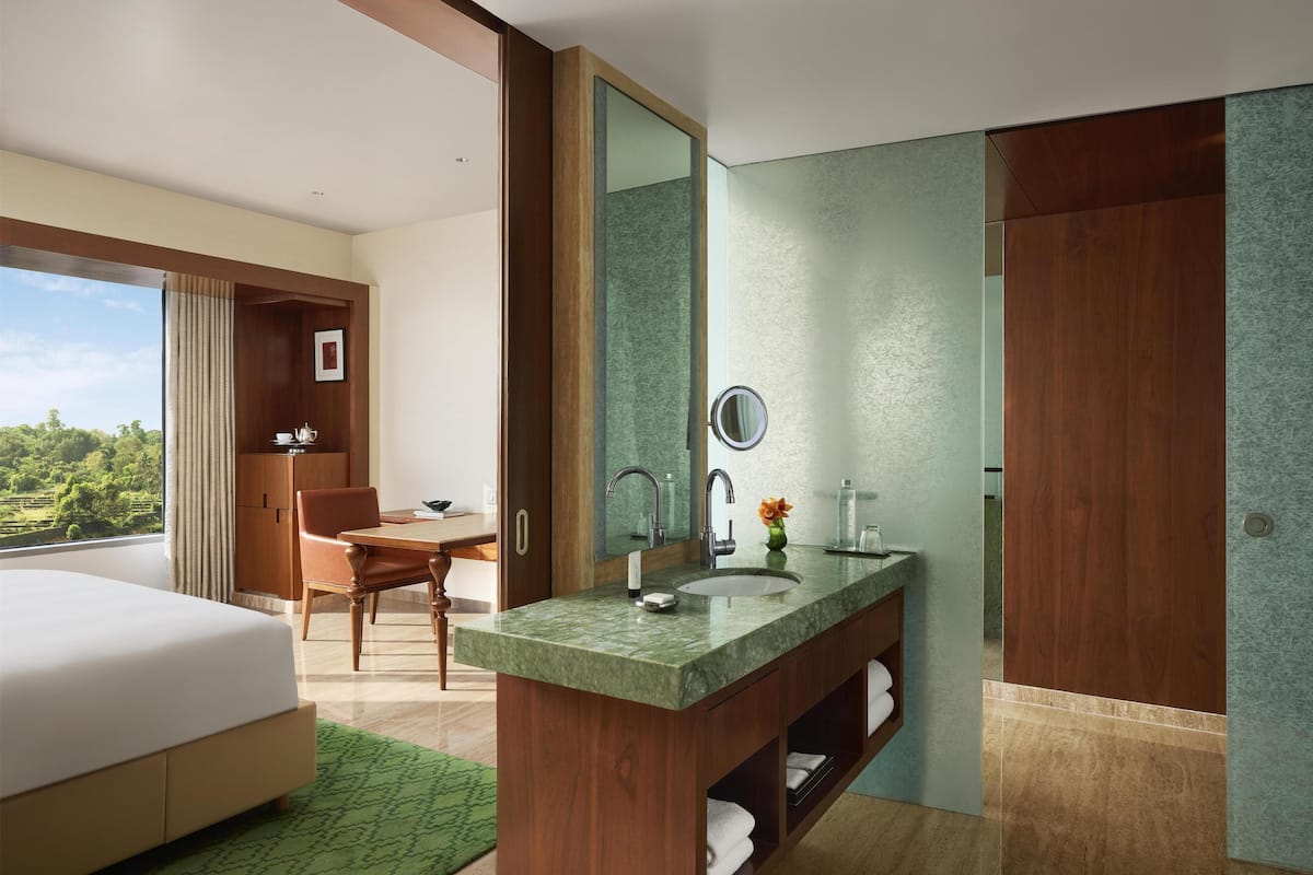 A hotel room with a bed, a desk, a bathroom with a large mirror, and a view of the outdoors.