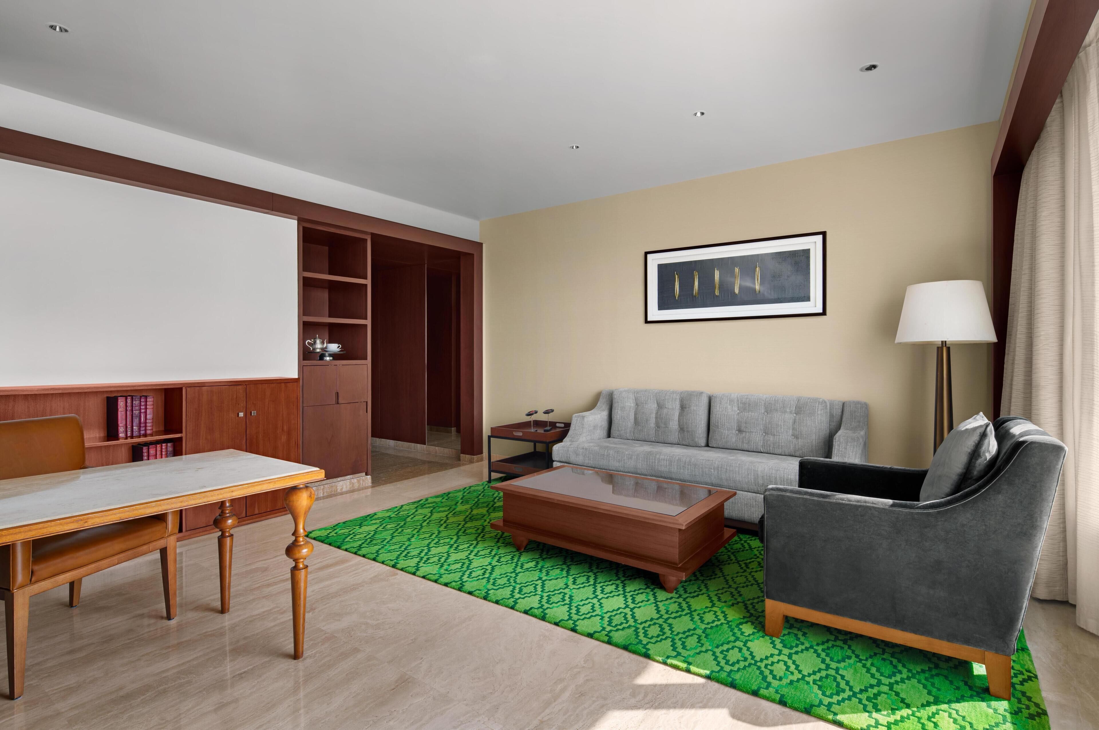 A modern living room with a sofa, coffee table, and a dining table. There is a bookshelf, a lamp, and a framed picture on the wall.