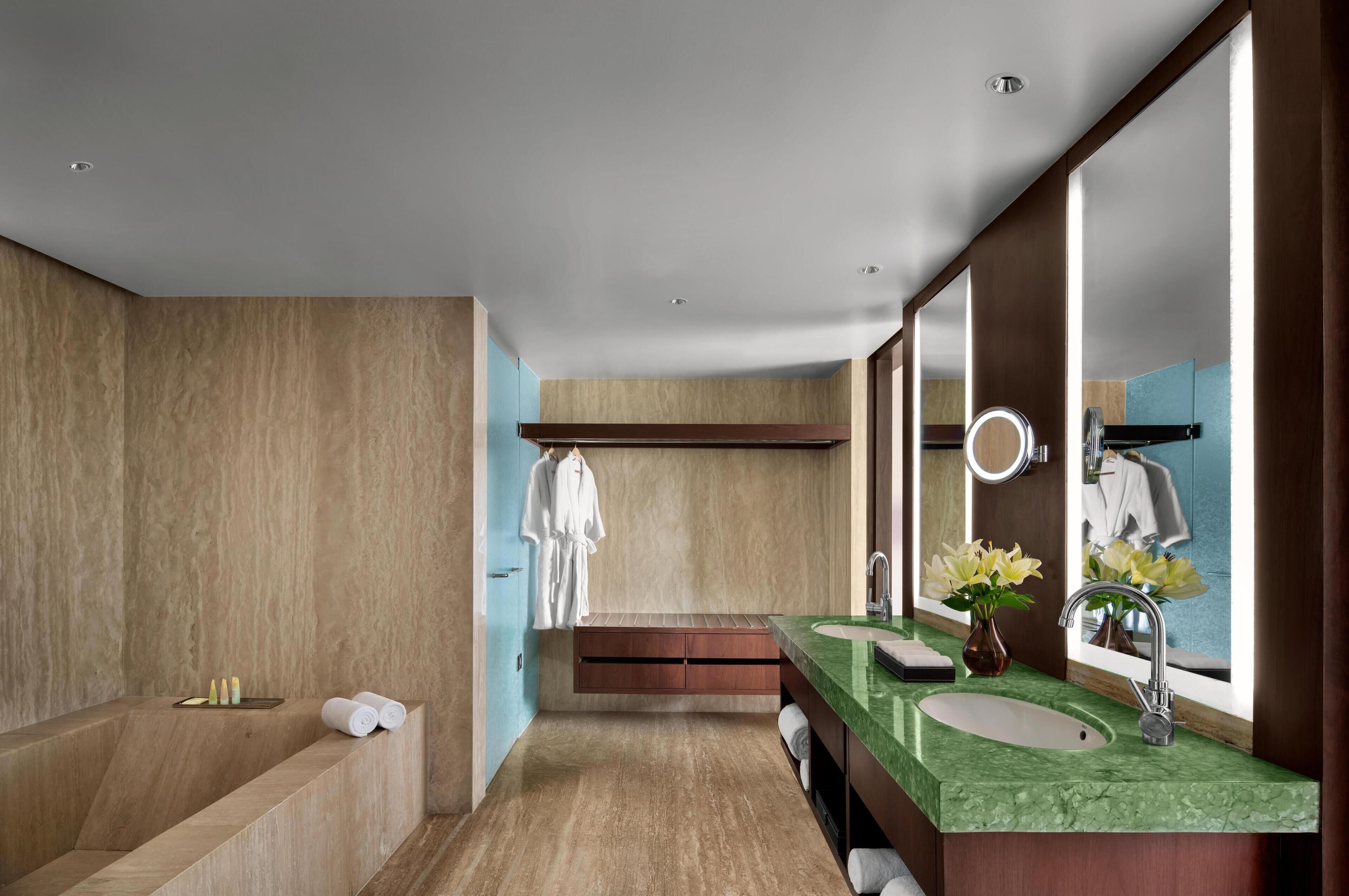 A modern bathroom with a large mirror, a bathtub, a vanity with a green countertop, and a window.