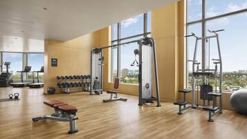 Un gimnasio espacioso con diversos equipos de ejercicio, ventanas amplias y vistas a la ciudad.