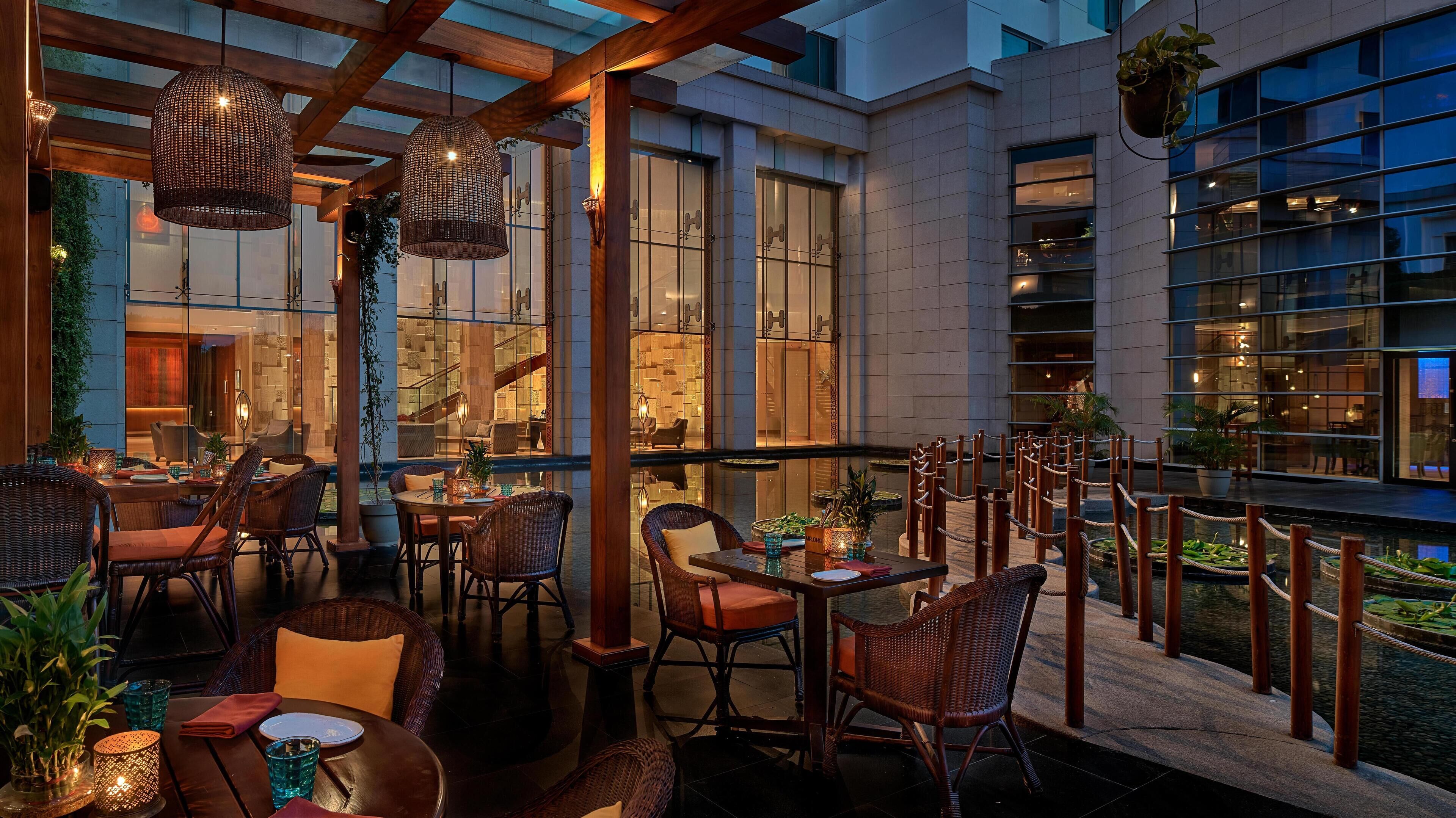 An indoor dining area with wicker furniture, a glass table, and a view of a building with large windows.