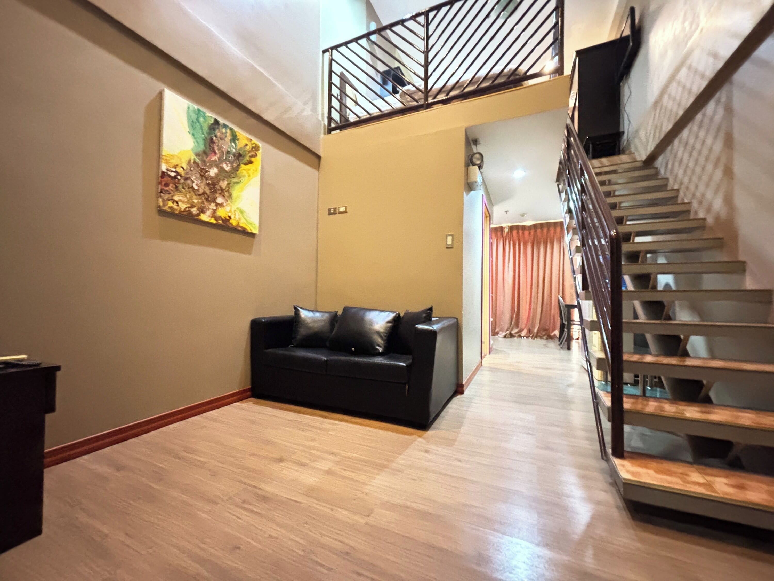 A living room with a black leather sofa, a staircase with wooden steps, and a painting on the wall.