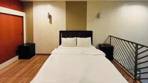 A hotel room with a bed, nightstands, a wooden floor, a red door, and a staircase. - Noorway Hotel and Residences (Cagayan de Oro)