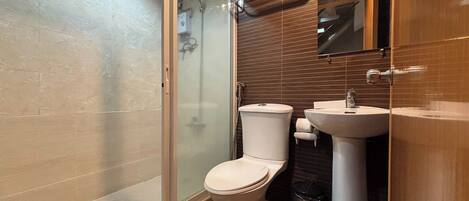 A bathroom with a glass-enclosed shower, a toilet, a sink, and a trash can.