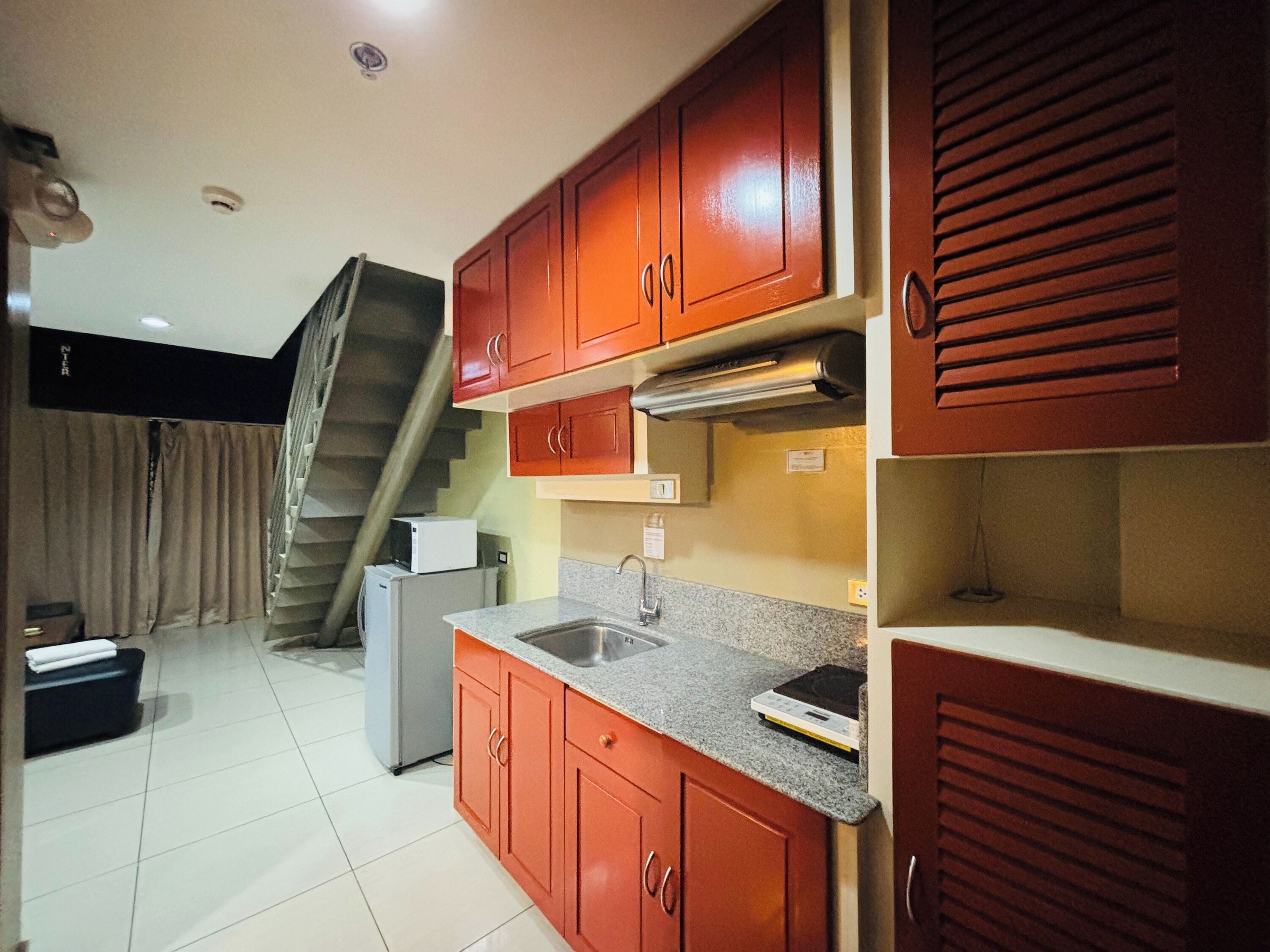 Cocina compacta con armarios rojos, un lavamanos de acero inoxidable y un microondas.