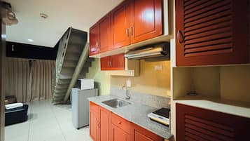 Cocina compacta con armarios rojos, un lavamanos de acero inoxidable y un microondas.