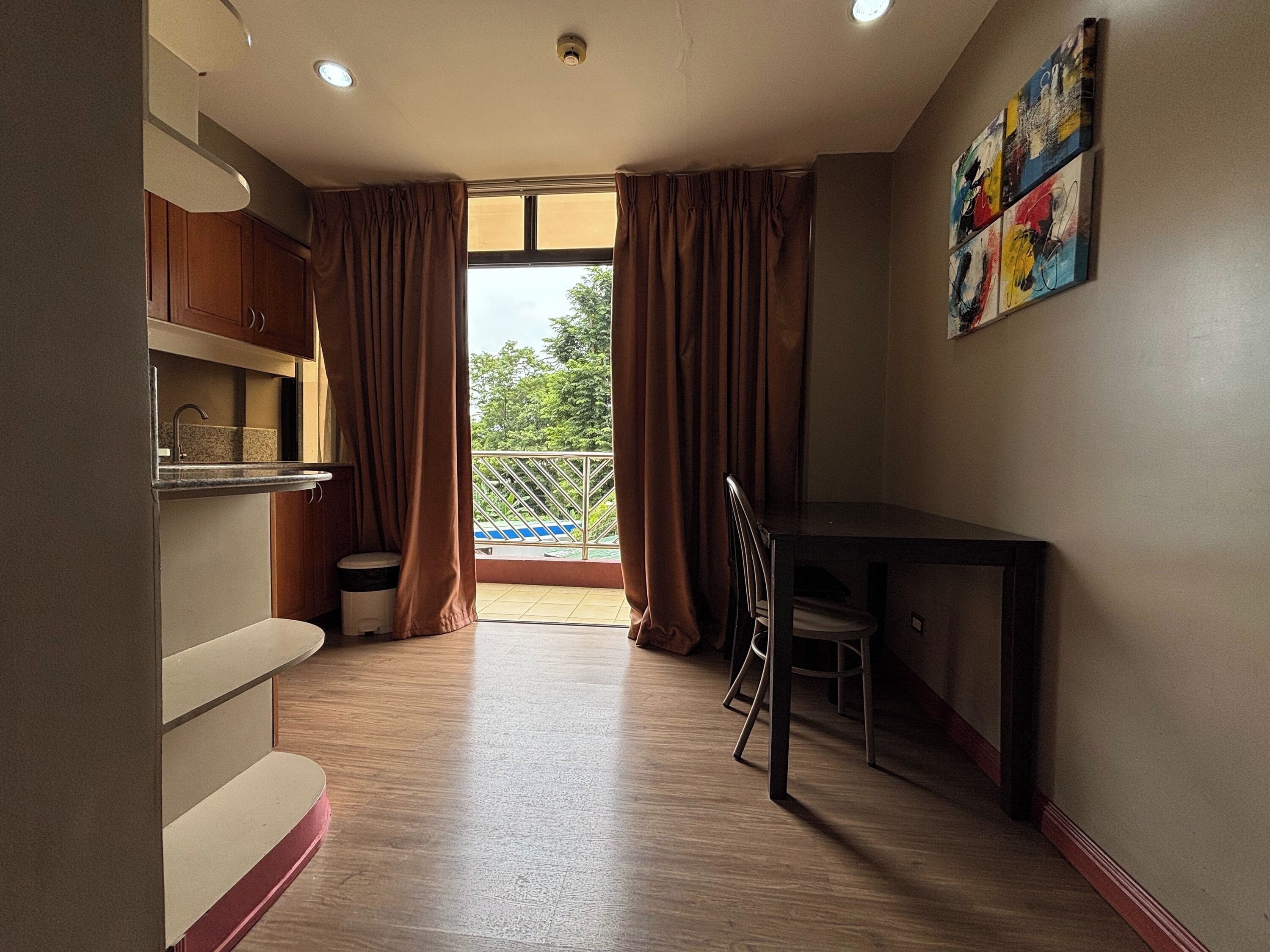 A room with a kitchen area, a dining table, and a view of a balcony with a railing.