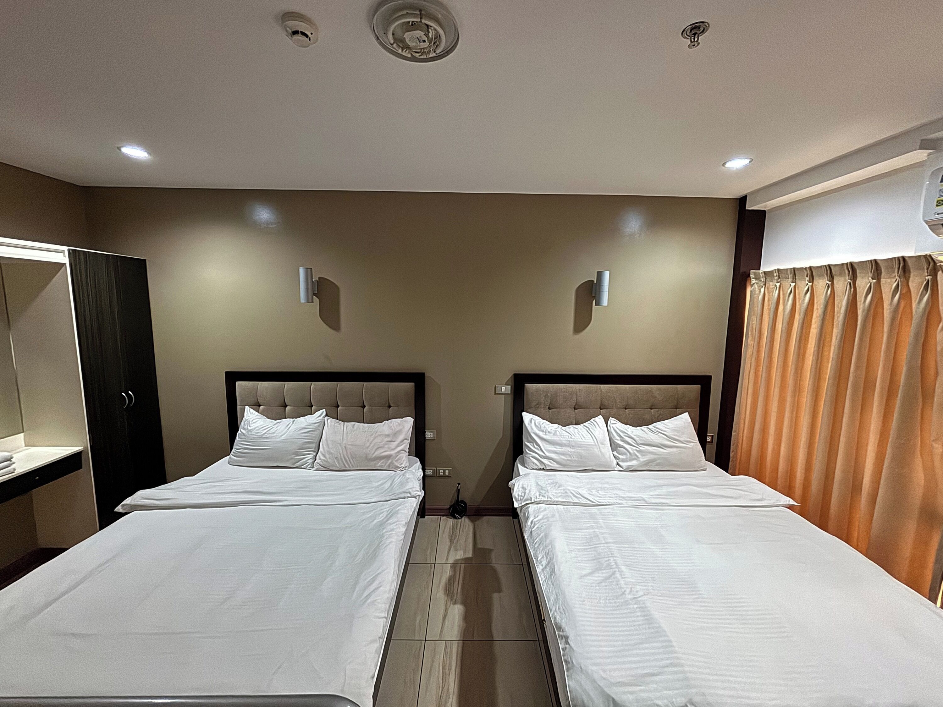 Une chambre d’hôtel avec deux lits, une armoire, un miroir et un rideau.