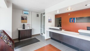 A hotel reception area with a modern design, featuring a reception desk, a coffee machine, and a digital display.