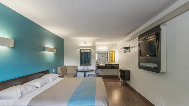 A hotel room with a bed, a desk, a mirror, and a TV.