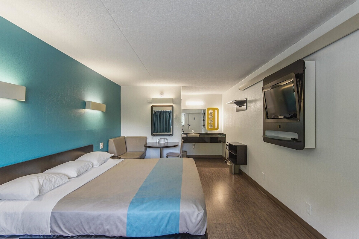 Une chambre d’hôtel avec un lit, un bureau, un miroir et une télévision.