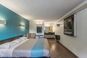 Une chambre d’hôtel avec un lit, un bureau, un miroir et une télévision.