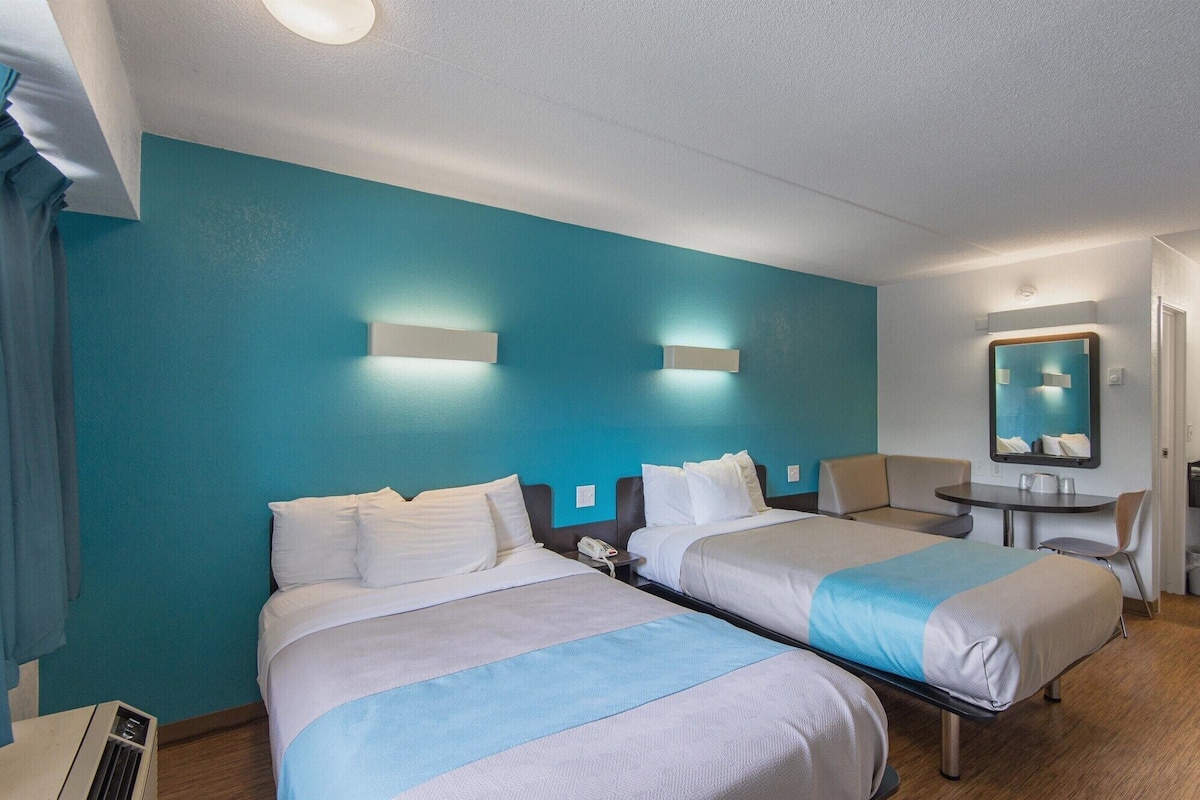 Une chambre d’hôtel avec deux lits, une petite table, une chaise, un miroir et un téléphone fixé au mur.