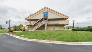 A motel with a prominent '6' sign, a staircase leading to the entrance, and a well-maintained lawn.