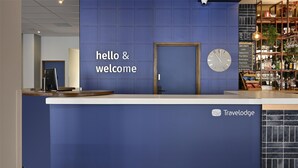 A reception desk with a blue wall, a clock, and a sign that reads "hello & welcome". - Travelodge London Woolwich (London)
