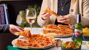 A dining table with pizza, a bottle of Stella Artois beer, a salad, and a wine glass. - Travelodge London Excel Hotel (London)